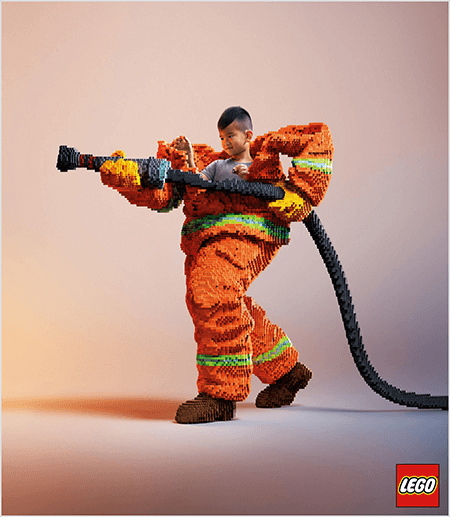 Dit is een foto uit een LEGO-advertentie waarop een jonge Aziatische jongen te zien is in een brandweeruniform van LEGO. Het uniform is oranje met een neongroene streep rond de manchetten van de jas en broek. De brandweerman staat met één voet naar achteren en houdt een brandslang vast, ook gemaakt van lego's. Het hoofd van de jongen verschijnt uit de bovenkant van het uniform, dat veel groter is dan hij en stopt rond de schouders. De foto is gemaakt tegen een effen neutrale achtergrond. Het LEGO-logo verschijnt in een rood vak rechtsonder. Talia Wolf zegt dat LEGO een geweldig voorbeeld is van een merk dat emotie gebruikt in advertenties.
